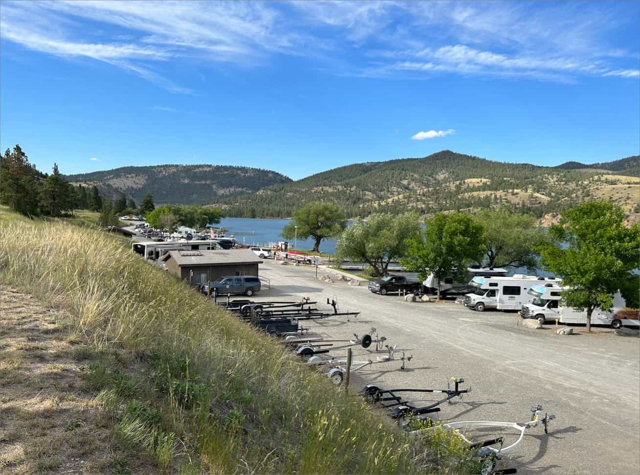 Recreational vehicles parked near a lake with boat trailers in the foreground and hills in the distance, at Black Sandy State Park, Montana.