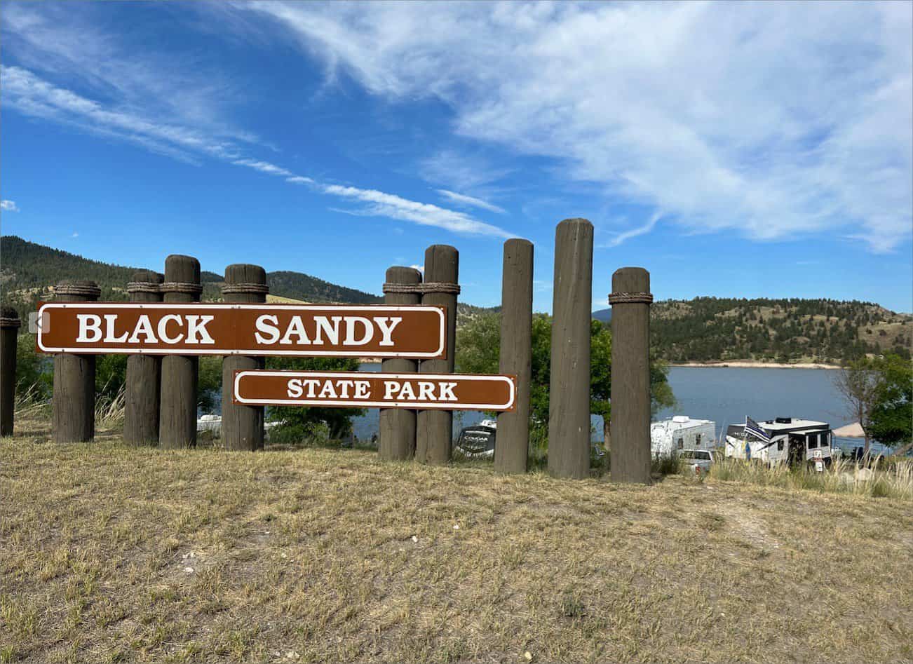 Entrance sign to Black Sandy State Park with a view of the lake and surrounding landscape in the background.