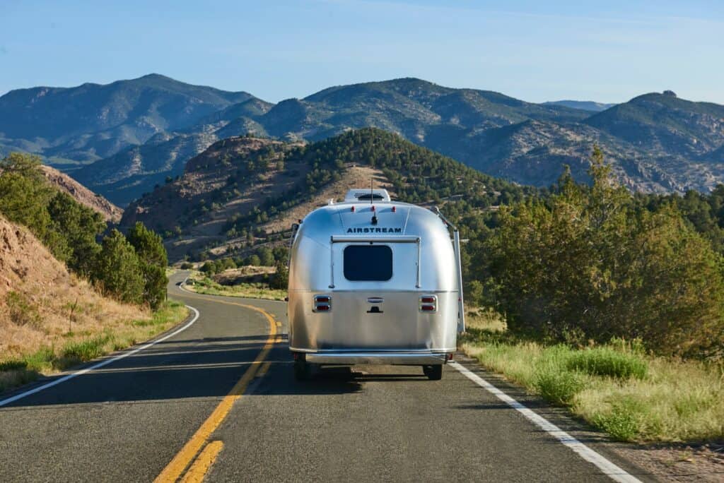 Airstream camper on two lane mountain road with foothills and mountains in the distance going camping
