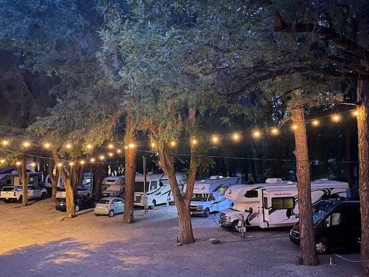 A group of RVs parked in a wooded area at night for camping in Ruidoso Village RV Park.